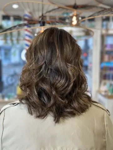 Balayage noisette sur cheveux châtain mi-longs, boucles souples
